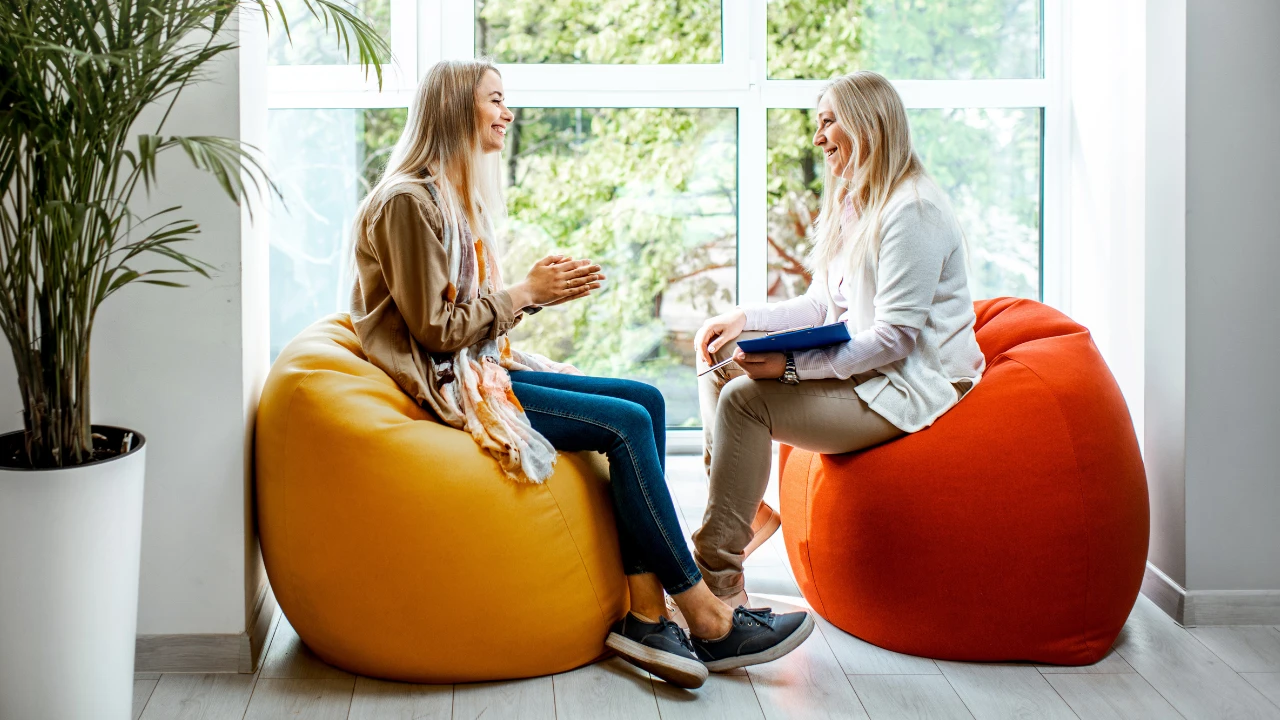 Coaching-tapaaminen: kaksi naista keskustelemassa valoisassa tilassa säkkituoleilla istuen.